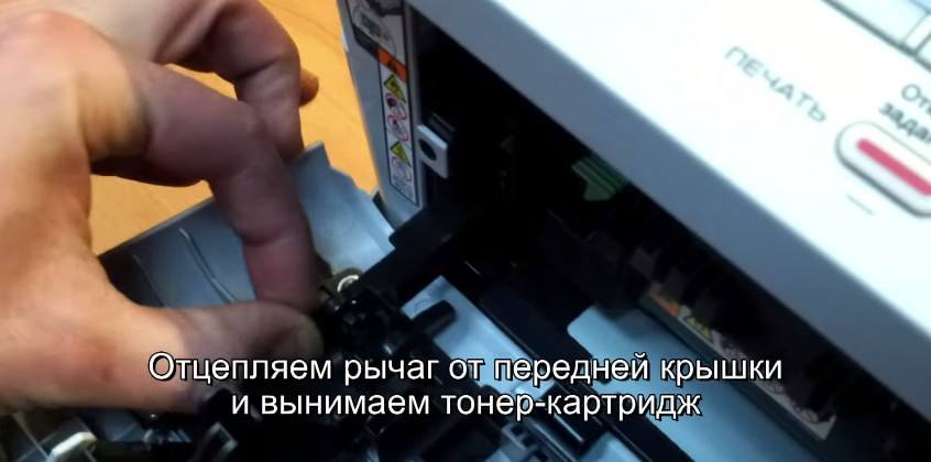 Отцепите рычаг от передней крышки в Brother HL-2130R Отцепите рычаг от передней крышки в Brother HL-2130R